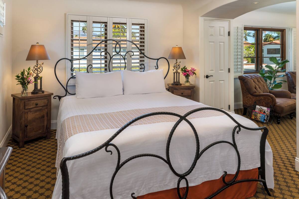 A neatly made bed with a white and orange bedspread, two bedside tables with lamps, and a chair with a magazine.
