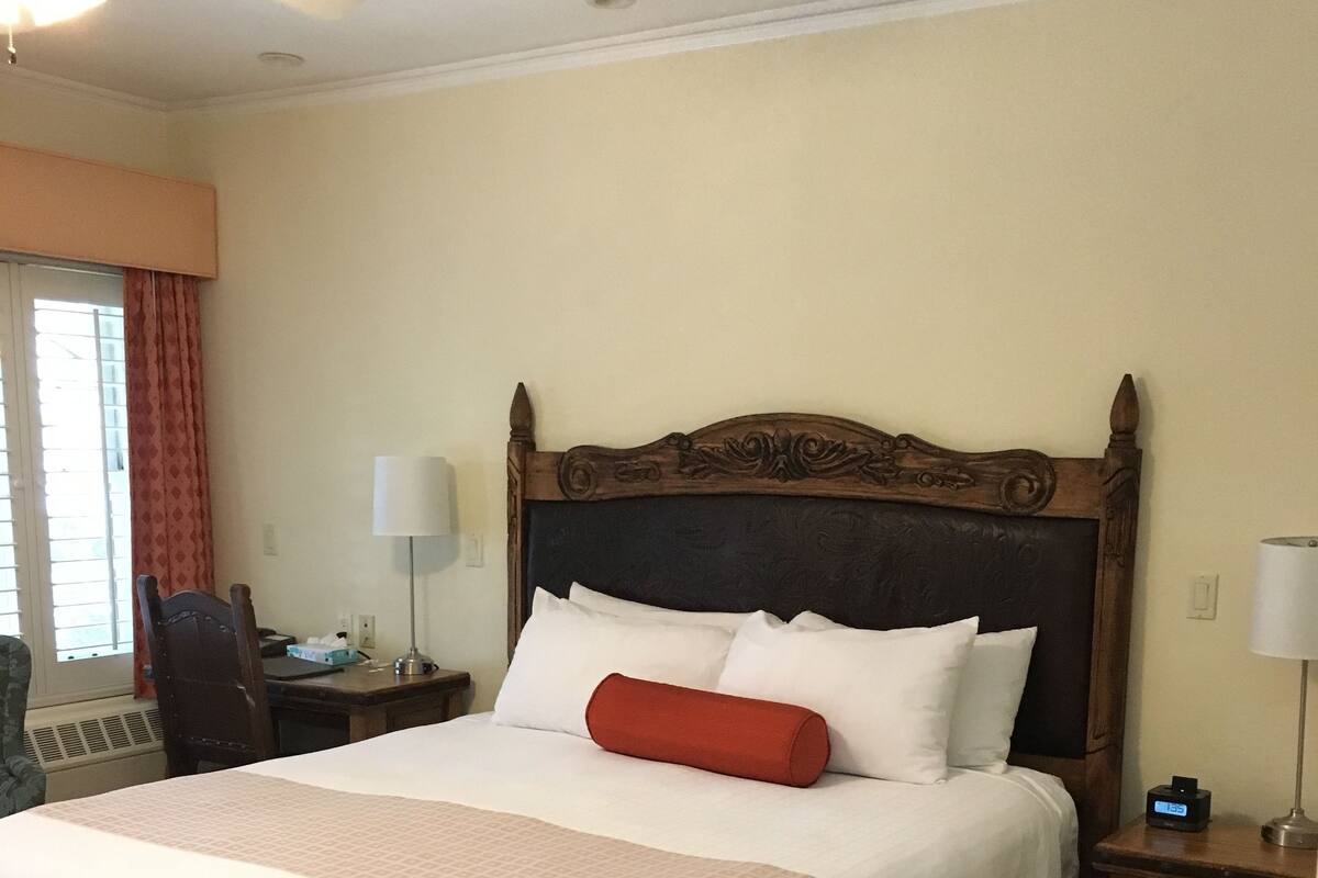 A hotel room with a large bed, a wooden headboard, a desk with a lamp, and a chair.