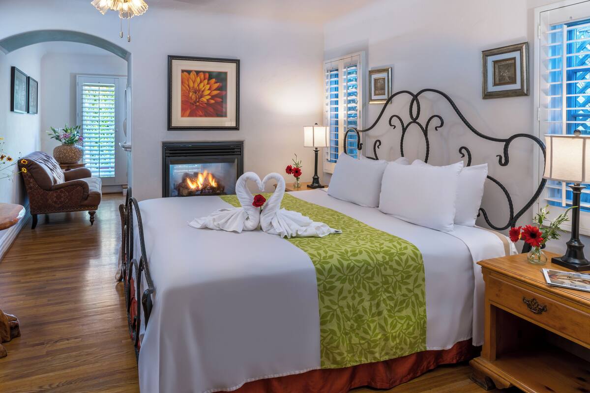 A hotel room with a large bed, a fireplace, a green bedspread, and a view of the outside through the window.