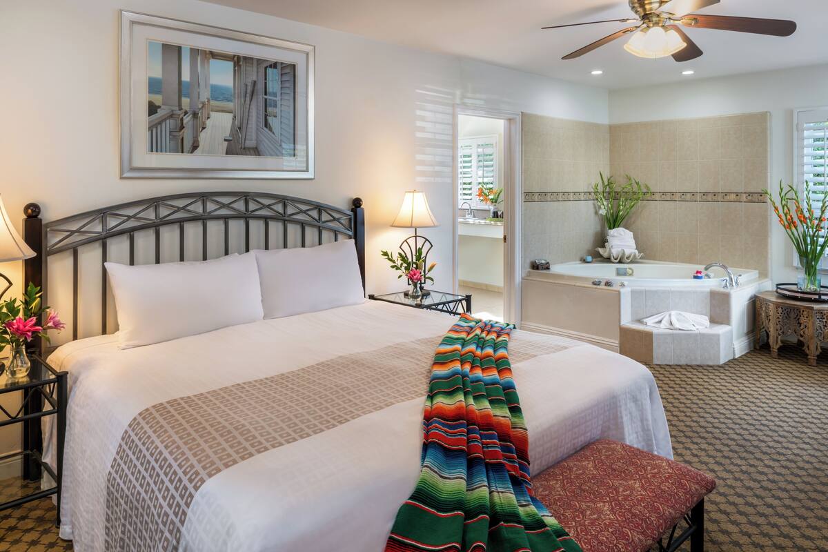 A hotel room with a large bed, a bathroom with a bathtub, and a ceiling fan.