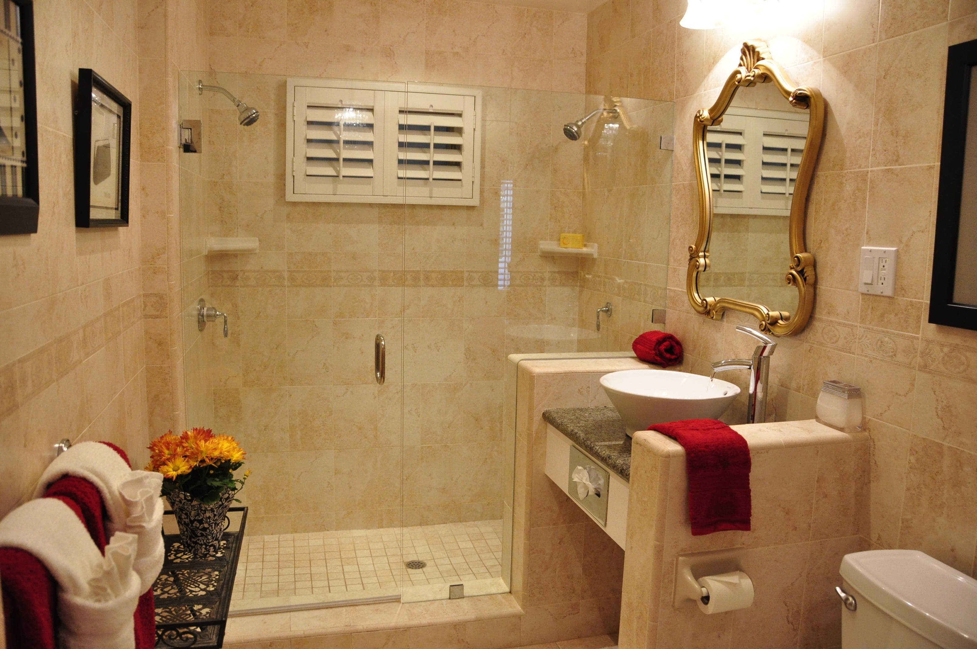 A bathroom with a glass-enclosed shower, a sink with a red towel, and a mirror with an ornate frame.