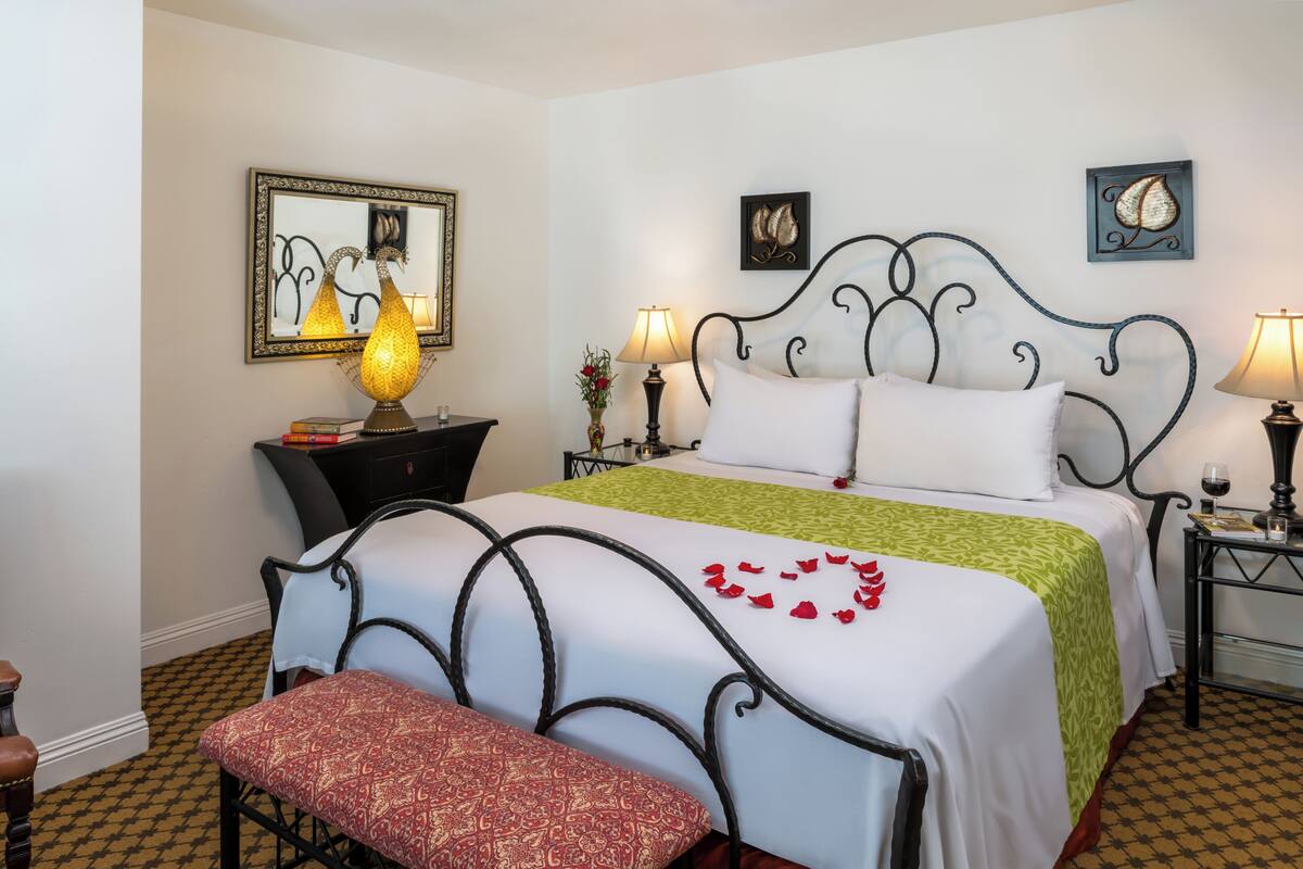 A neatly arranged bedroom with a bed, bedside tables, lamps, and a bench.