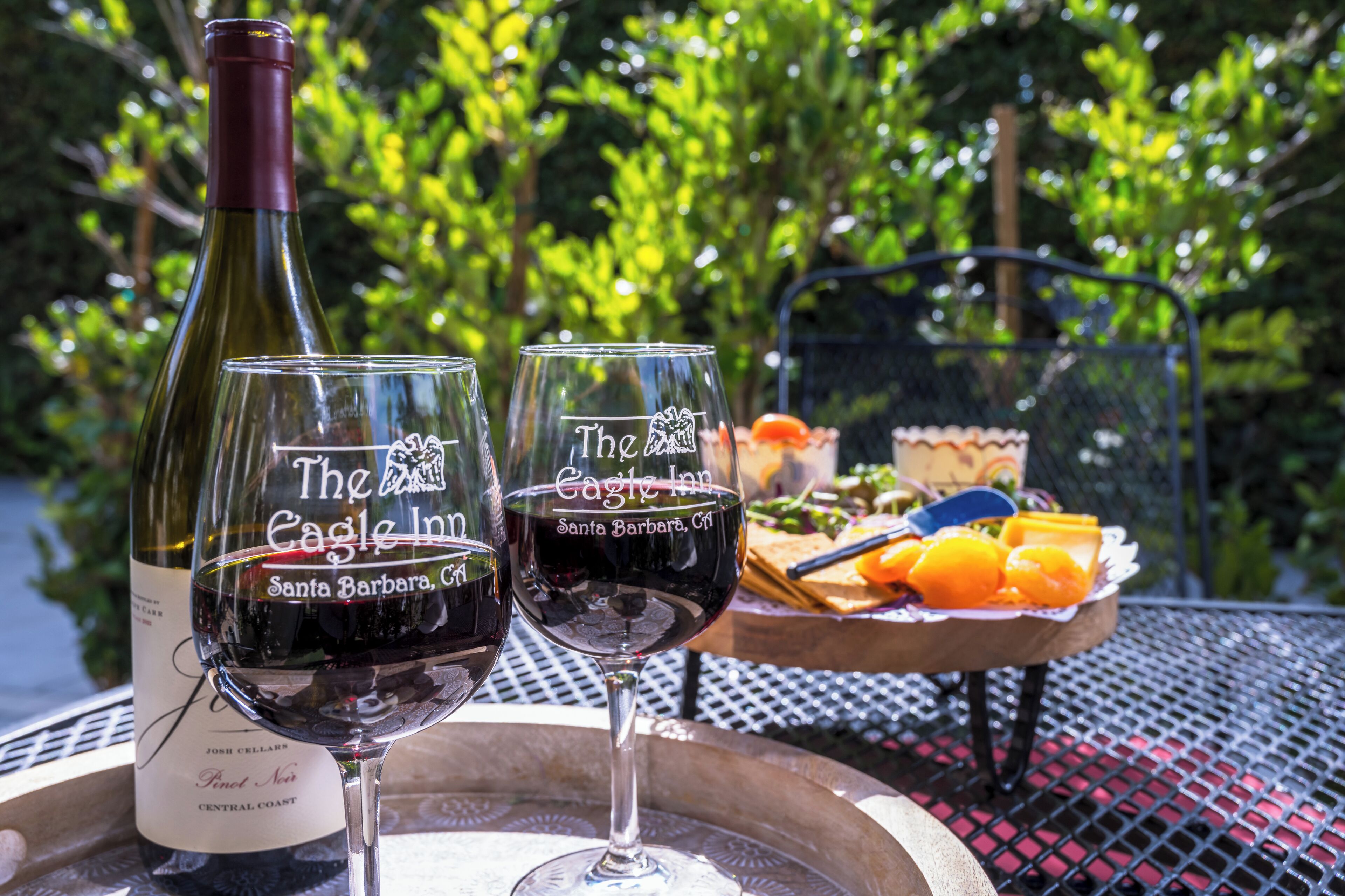 Two wine glasses and a bottle on a table with a tray of fruit and a basket in the background.