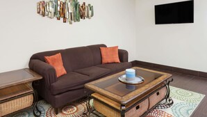 Ein Wohnzimmer mit einem braunen Sofa, orangefarbenen Kissen, einem Couchtisch mit Glasplatte, Körben aus Weidengeflecht und einem gemusterten Teppich.