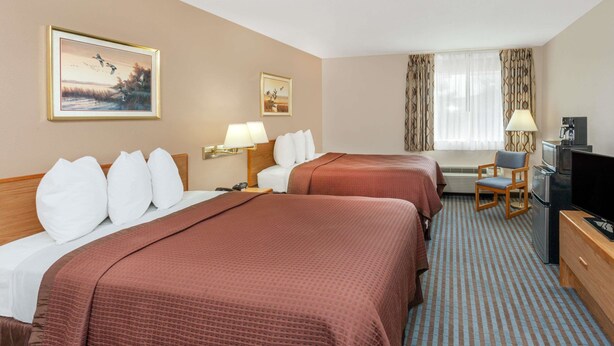 Ein Hotelzimmer mit zwei Betten, einem Schreibtisch mit Fernseher und einem Fenster mit Vorhängen.