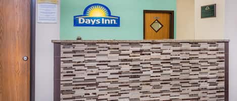 Uma receção com o logótipo Days Inn, uma porta de madeira e uma placa afixada na parede.