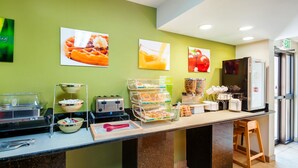 A breakfast bar with waffle and juice dispensers, a refrigerator, and a trash bin.