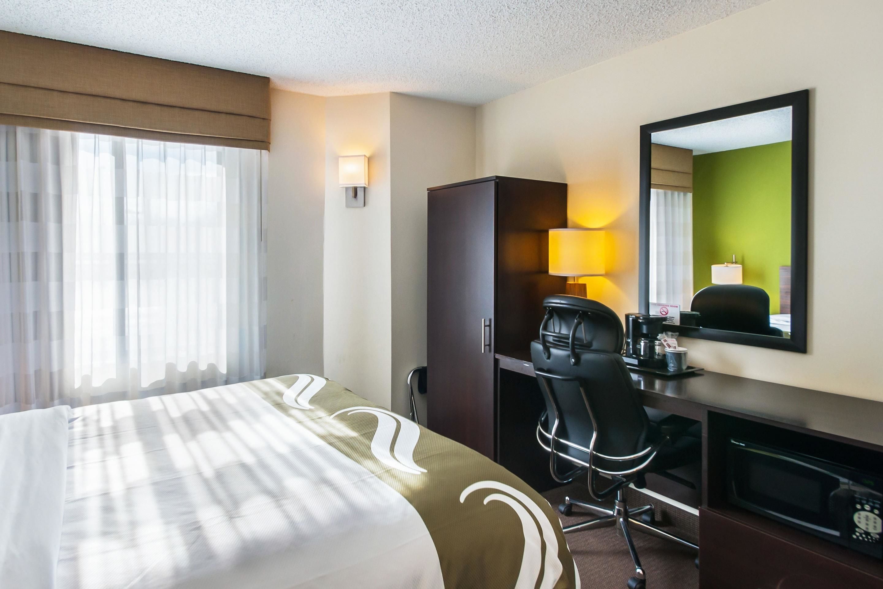 A hotel room with a bed, a desk, a chair, a television, and a mirror.