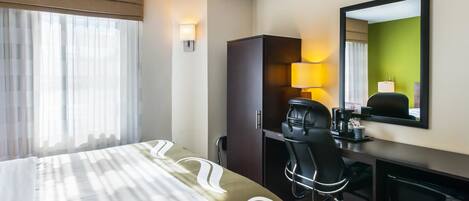 Une chambre d’hôtel équipée d’un lit, d’un bureau, d’une chaise, d’une télévision et d’un miroir.
