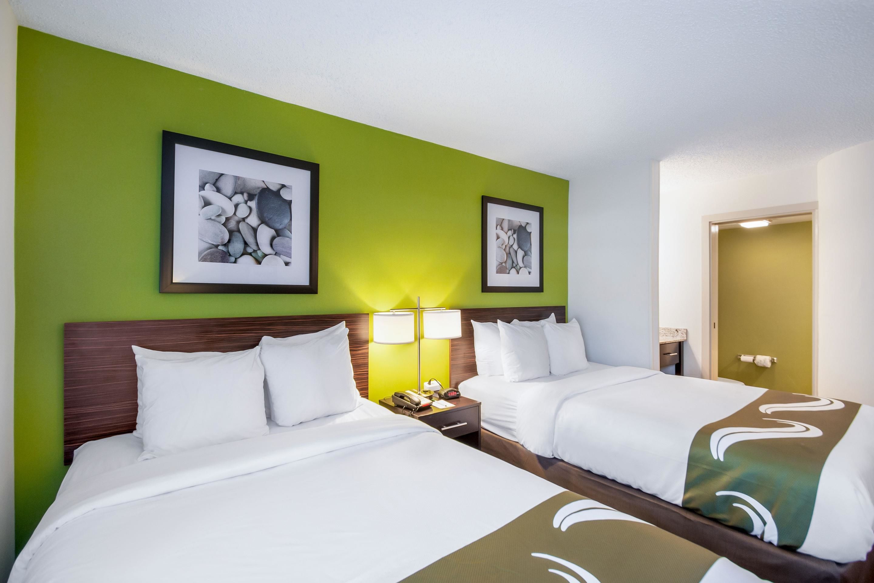 A hotel room with two beds, green walls, framed artwork, bedside lamps, and a wooden headboard.