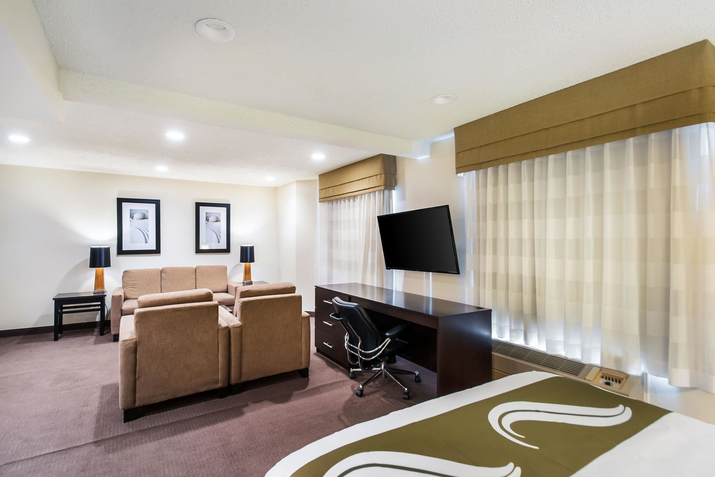 A hotel room with a bed, a desk, a chair, a sofa, and a TV.