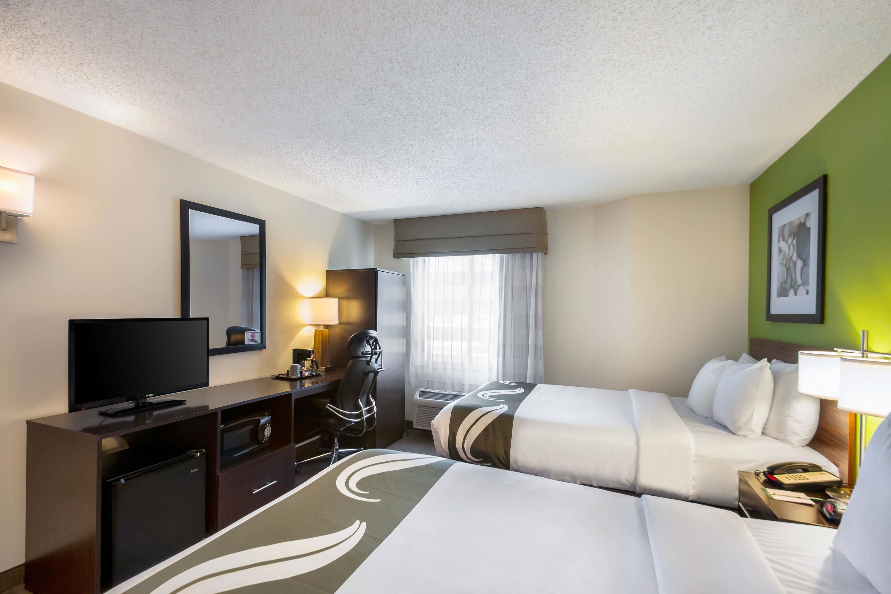 A hotel room with two beds, a desk with a television, a chair, a desk lamp, a telephone, and a window with curtains.
