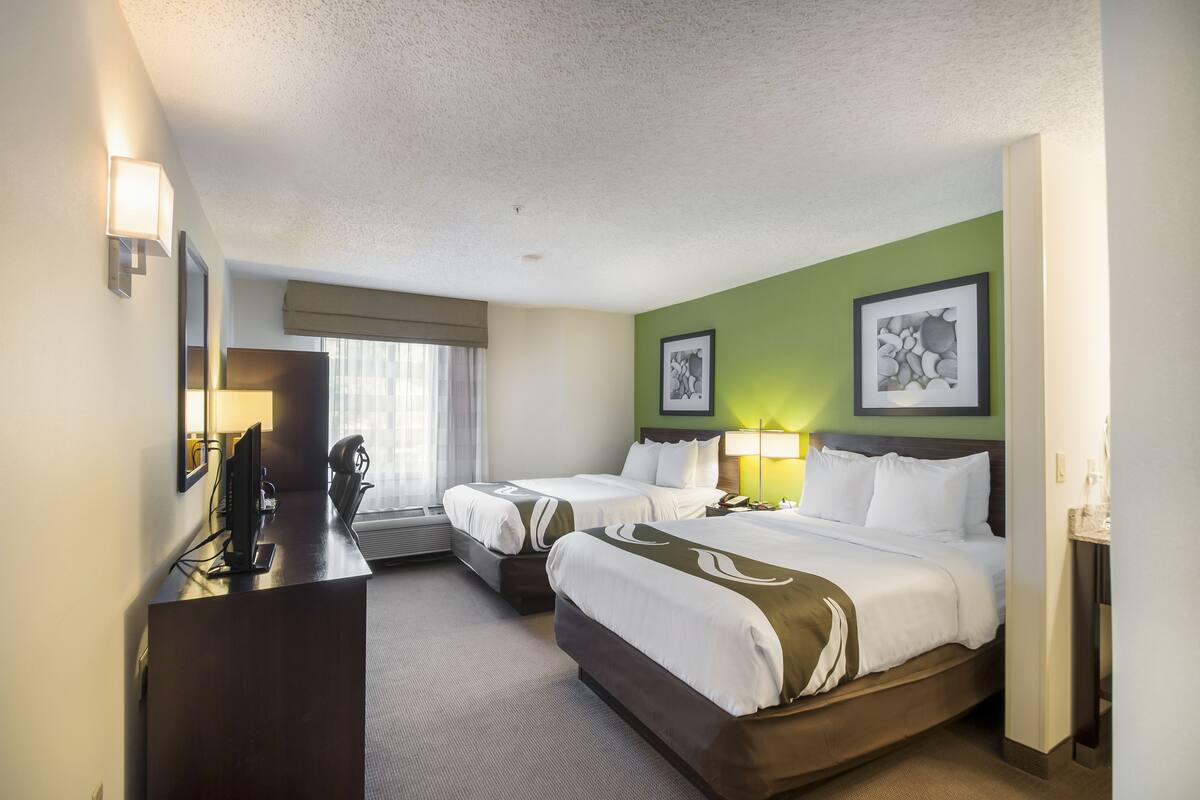 A hotel room with two beds, a desk, a computer, and a window with curtains.