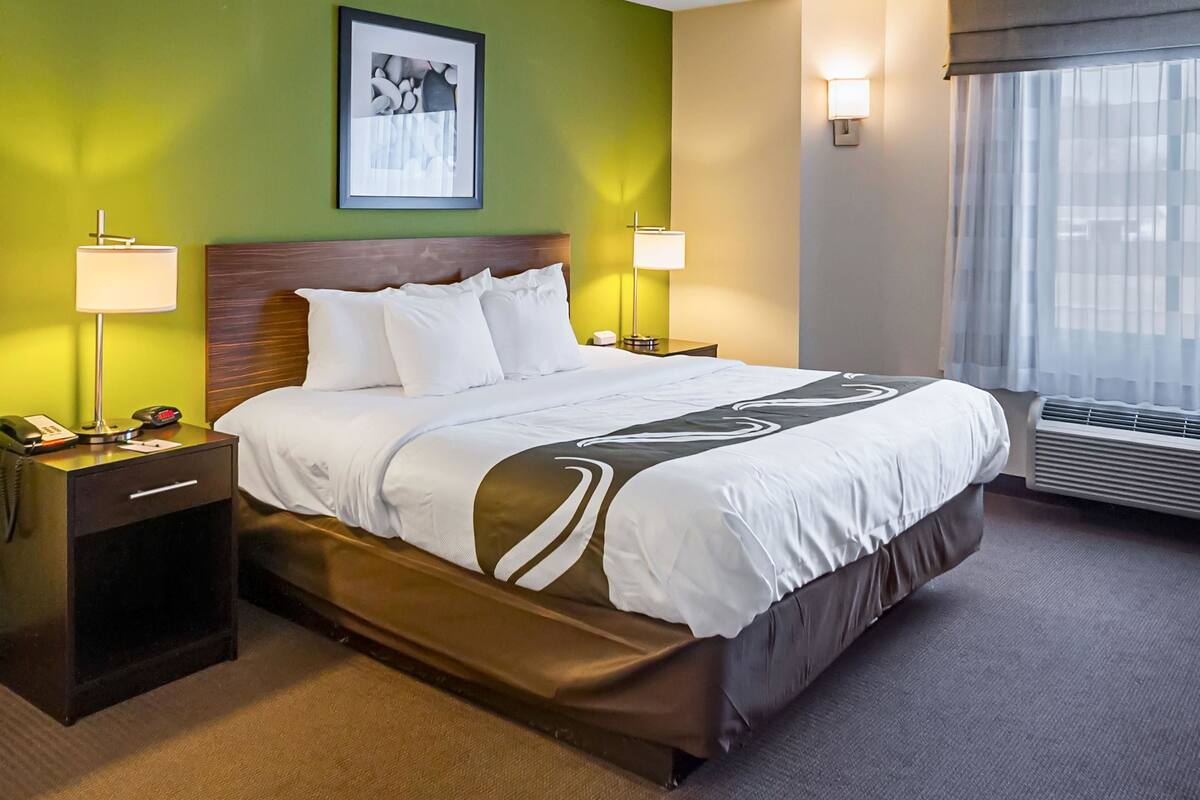 A hotel room with a large bed, two bedside lamps, a nightstand with a phone, and a framed picture on the wall.