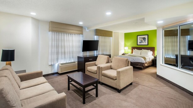 A hotel room with a sofa, armchairs, a TV, a bed, and a large window.