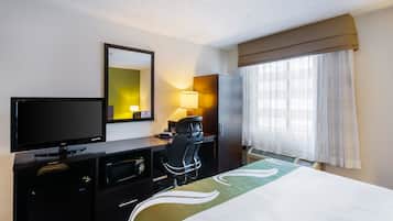 Una habitación de hotel con una cama, un escritorio con una computadora, un televisor y un espejo.