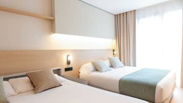 Habitación de hotel con dos camas, cabecera con iluminación integrada, ventana con cortinas y un aplique de pared.