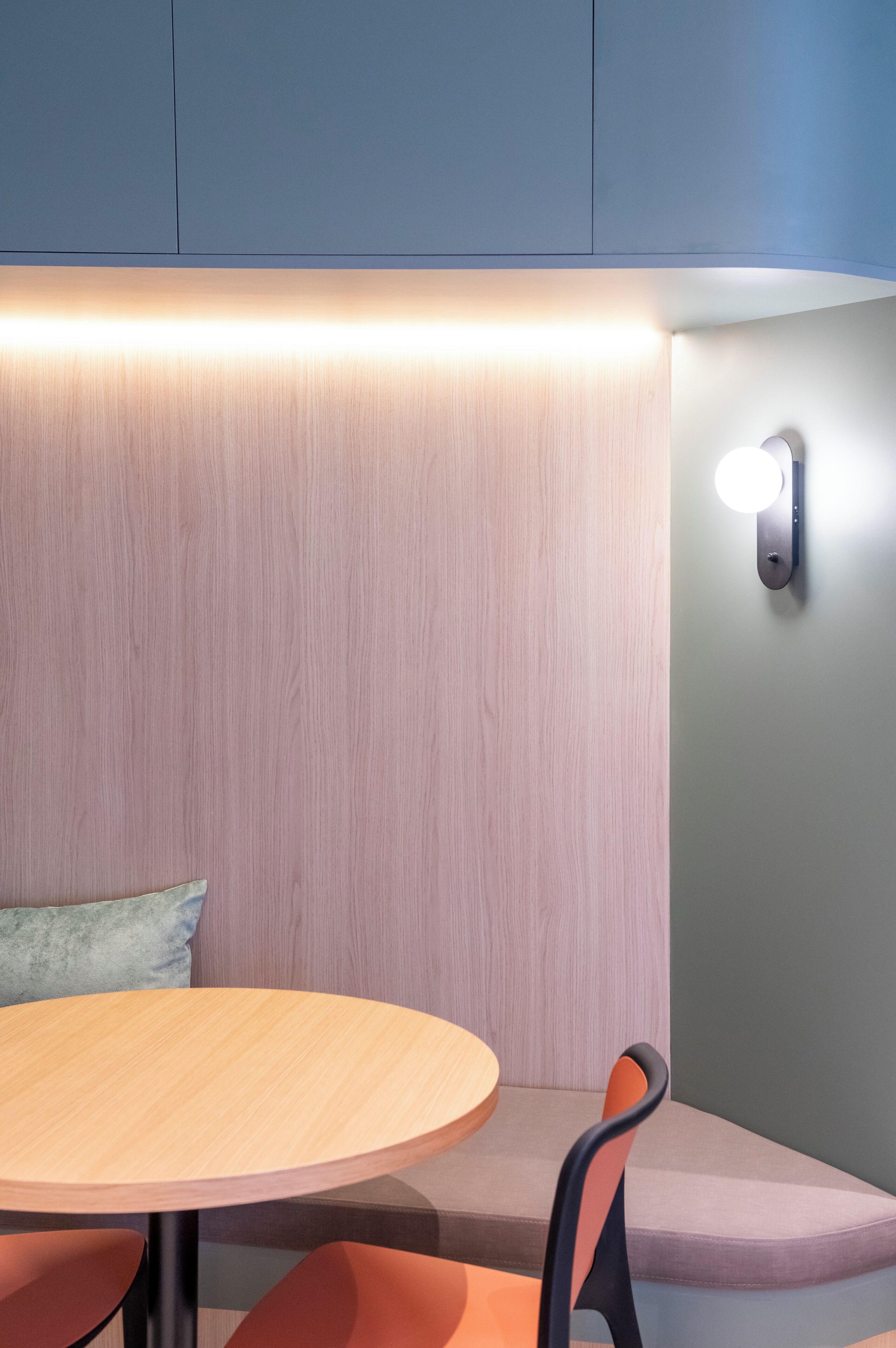A modern seating area with a round table, cushioned bench, and a wall-mounted light fixture.