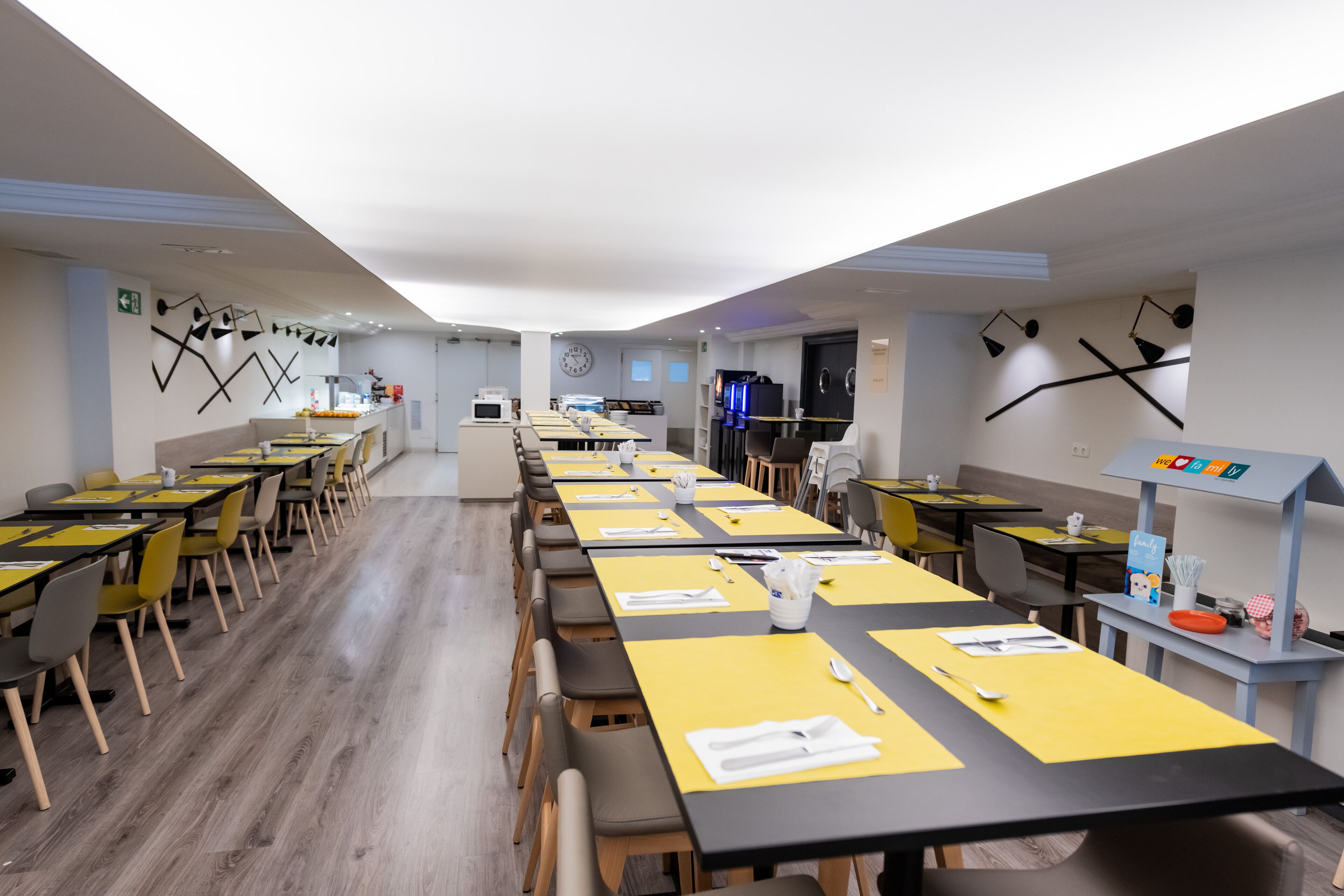 A modern dining area with long tables, yellow placemats, and black chairs.
