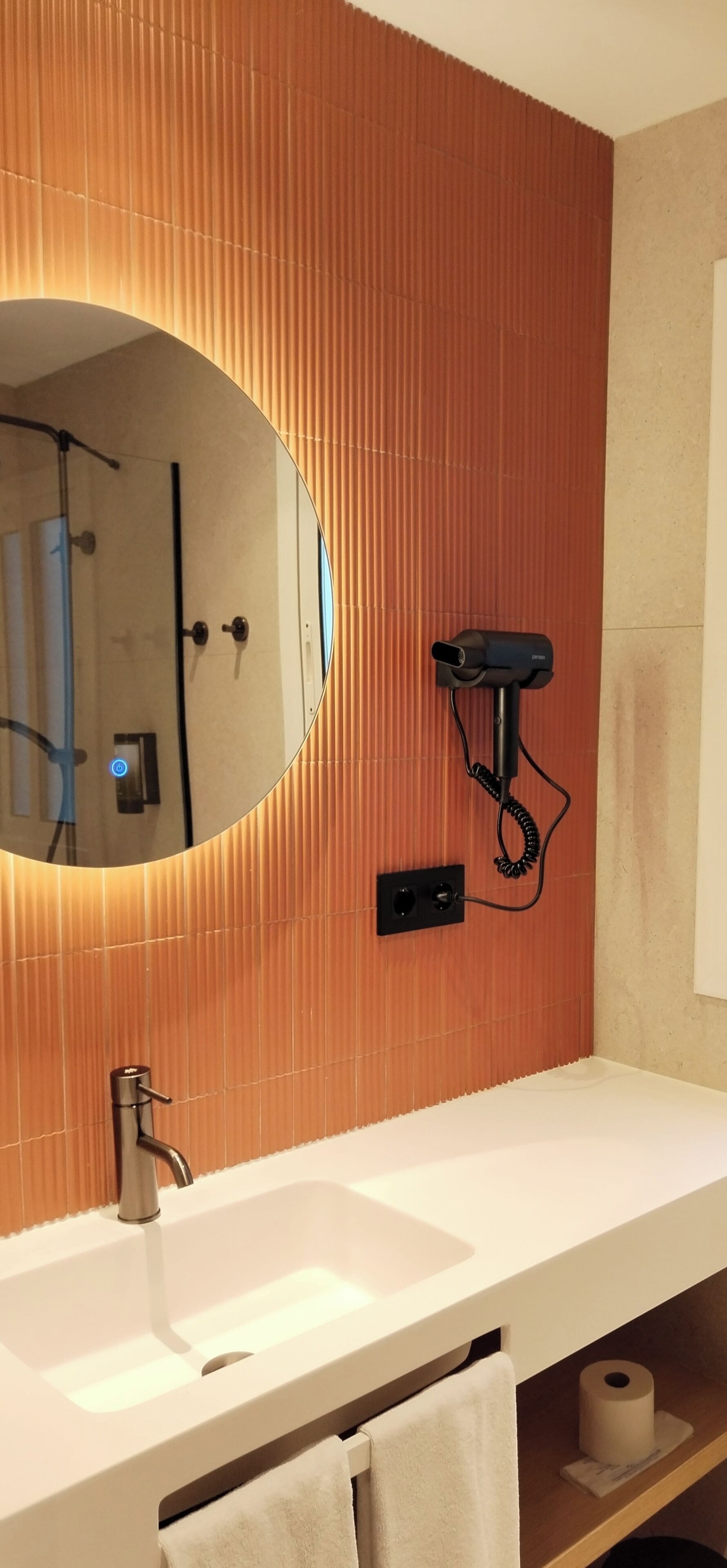 Ein Badezimmer mit einem weißen Waschbecken, einem Spiegel und einem an der Wand befestigten Föhn.