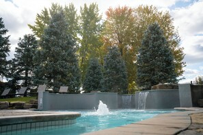 A swimming pool with a waterfall feature, surrounded by trees and lounge chairs.