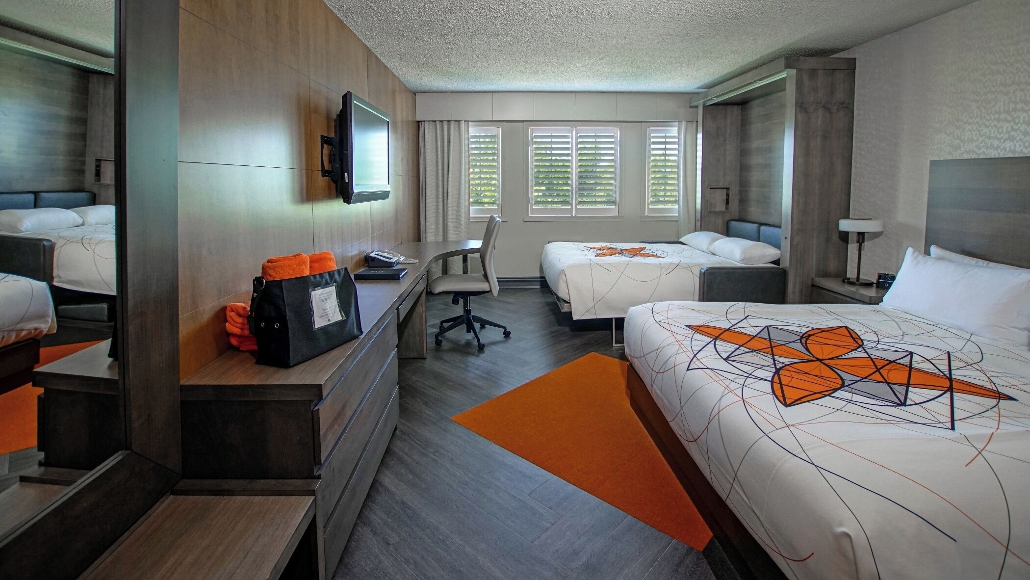 A hotel room with two beds, a desk, a chair, a TV, and a window with blinds.