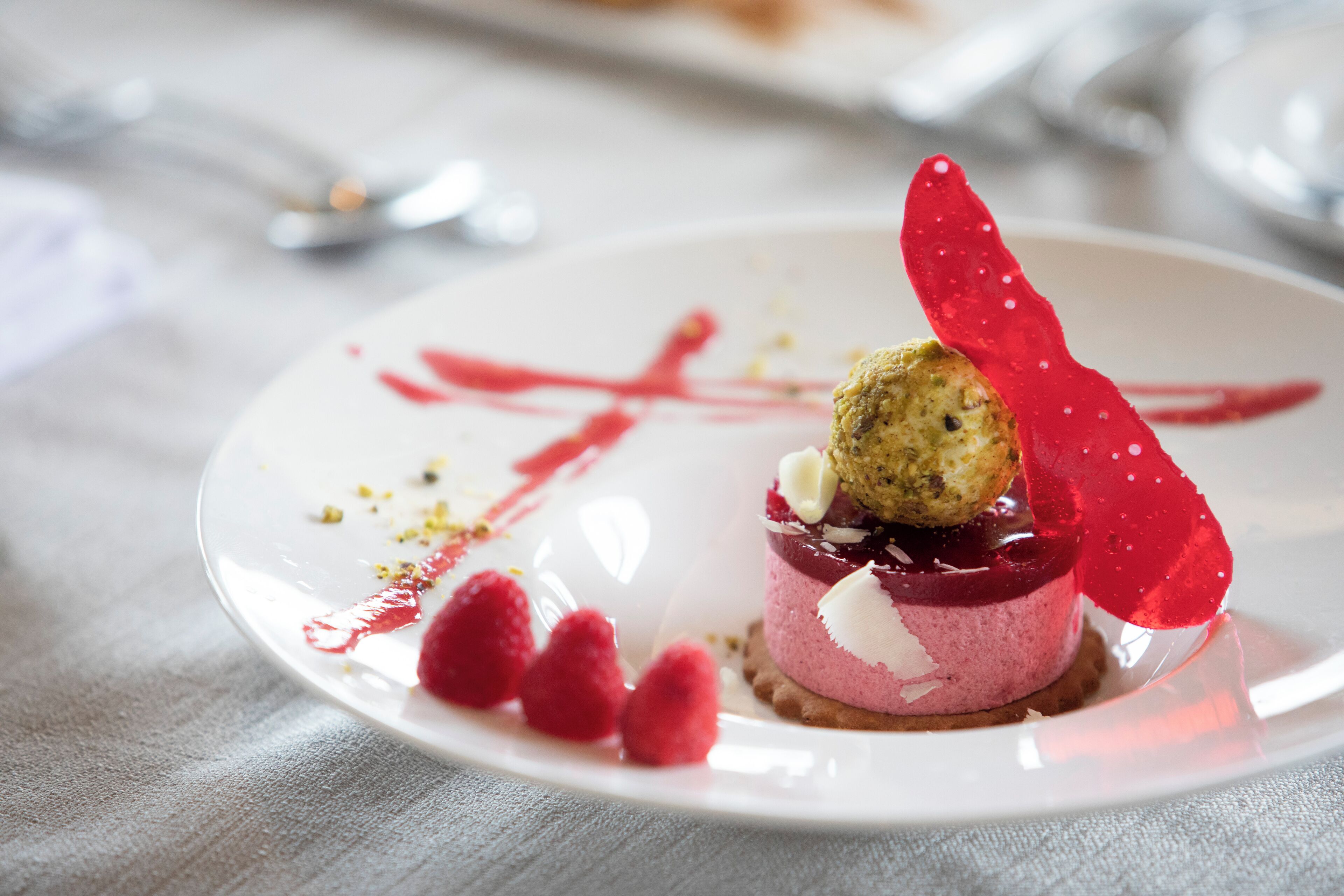 A dessert on a white plate with a red sauce design, raspberries, and a white cream topping.