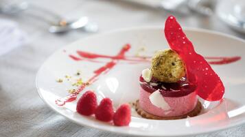 A dessert on a white plate with a red sauce design, raspberries, and a white cream topping.