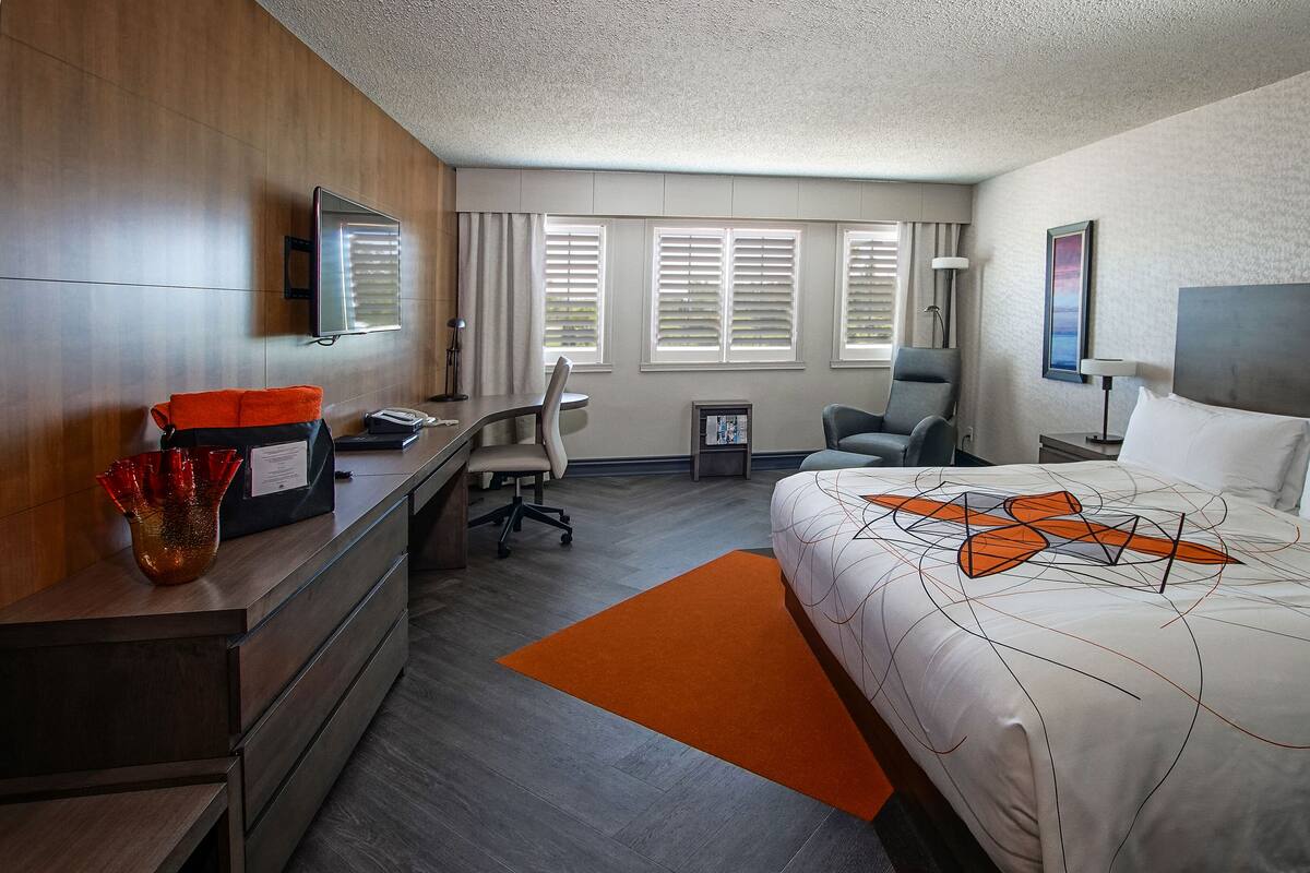 Quarto de hotel com cama, escrivaninha, cadeira e uma pequena mesa com abajur.