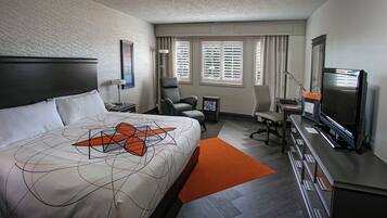 A hotel room with a large bed, a desk with a computer, a chair, a TV, and a window with blinds.