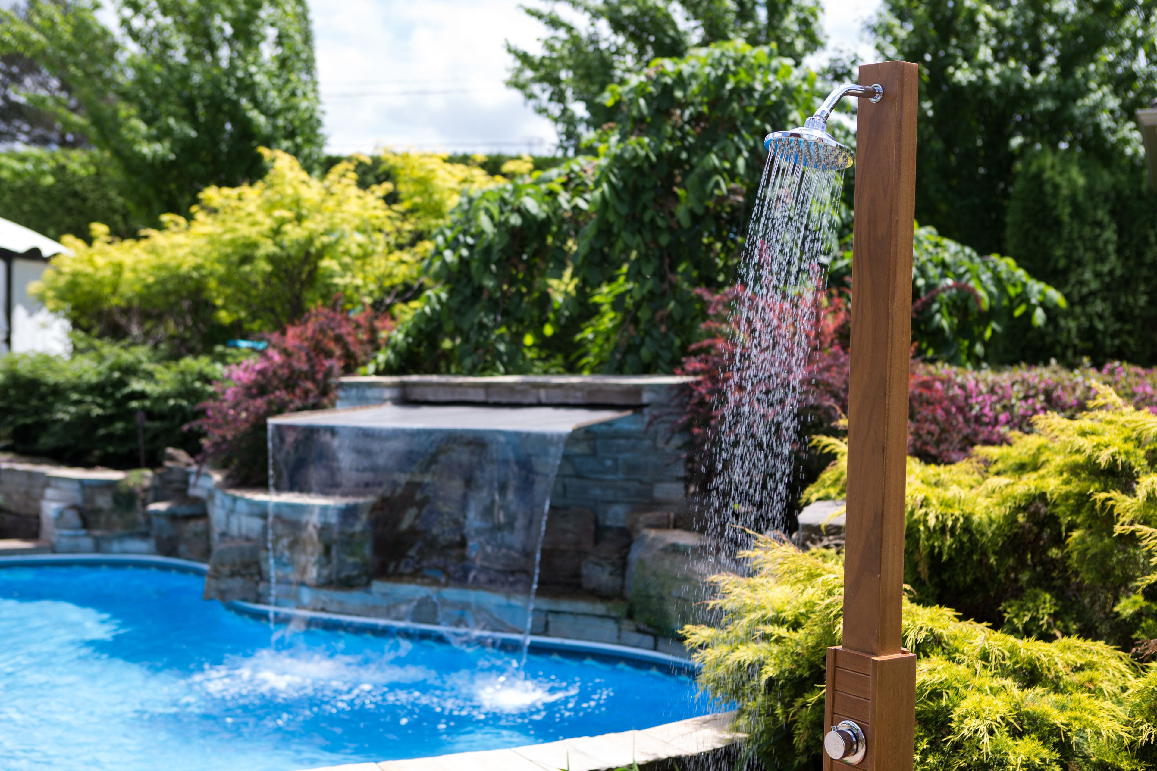 A wooden structure with a water feature, a stone waterfall, and a pool surrounded by lush greenery.