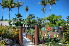 A pathway leading to a sign that reads "Kids Village" surrounded by palm trees and colorful flowers. - Vomo Island Resort (Vomo Island)