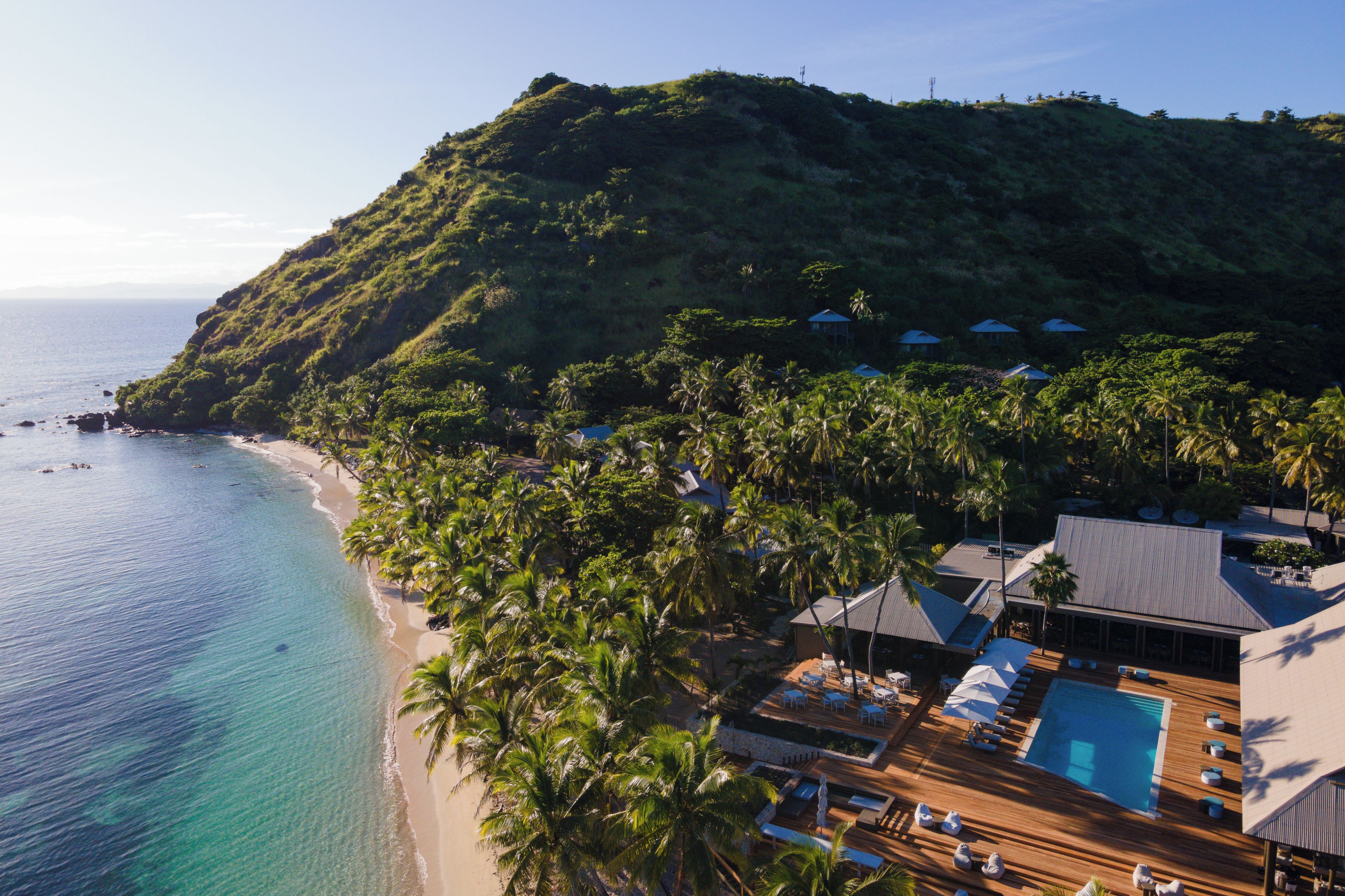 A resort with a pool area, beach, and tropical vegetation.