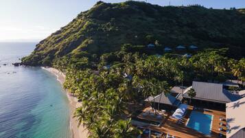 A resort with a pool area, beach, and tropical vegetation.