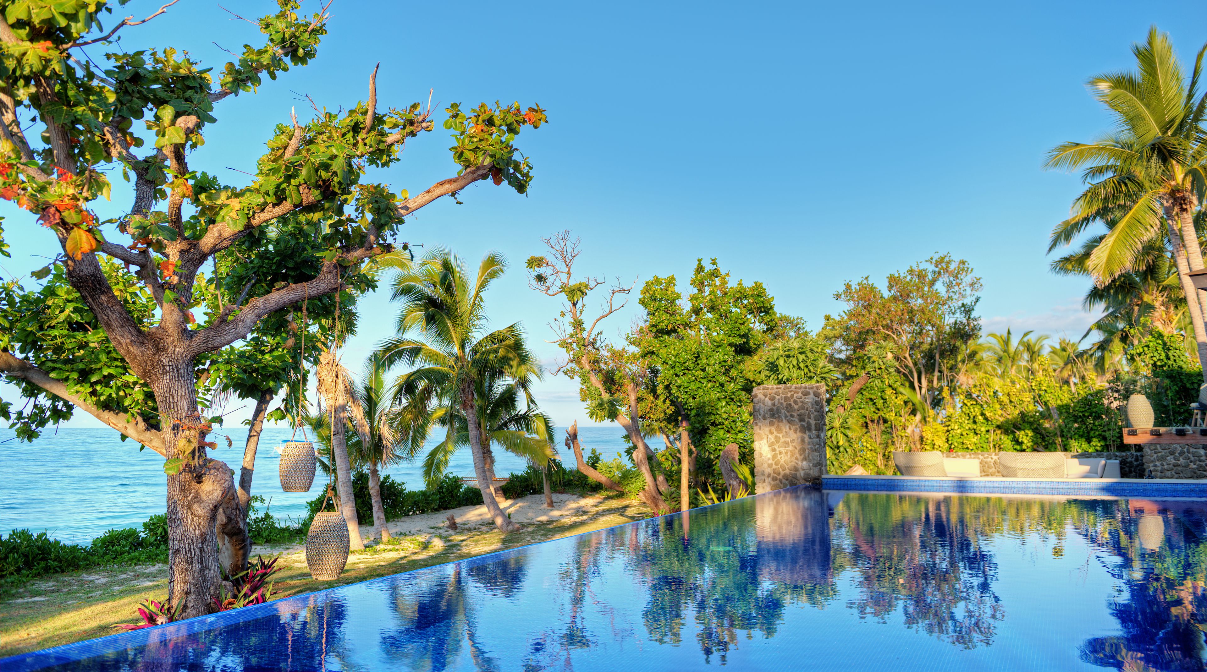 Una piscina con vista despejada al océano, rodeada de árboles tropicales y una estructura de piedra.