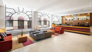 Un vestíbulo amplio con mostrador de recepción, sofás y un ventanal con vistas a un edificio de arcos.