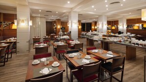 Un comedor de hotel con varias mesas y sillas, un mostrador de buffet y una escalera que sube a un nivel superior.