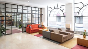 Un moderno vestíbulo de hotel con un amplio ventanal, un sofá rojo, un sofá beige, una mesa de centro de madera y una planta en maceta.