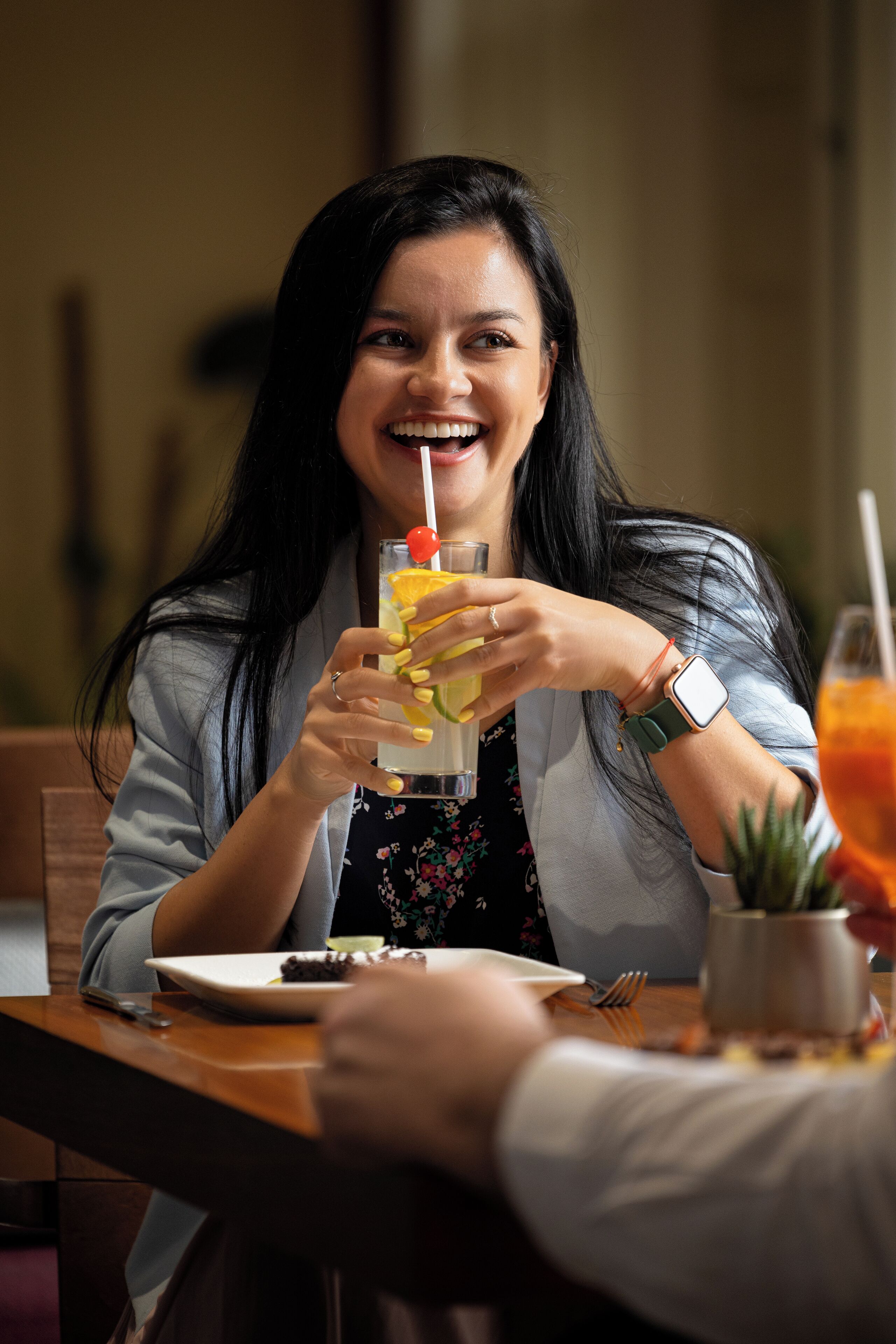Una persona seduta a un tavolo con una bevanda e un piatto di cibo.