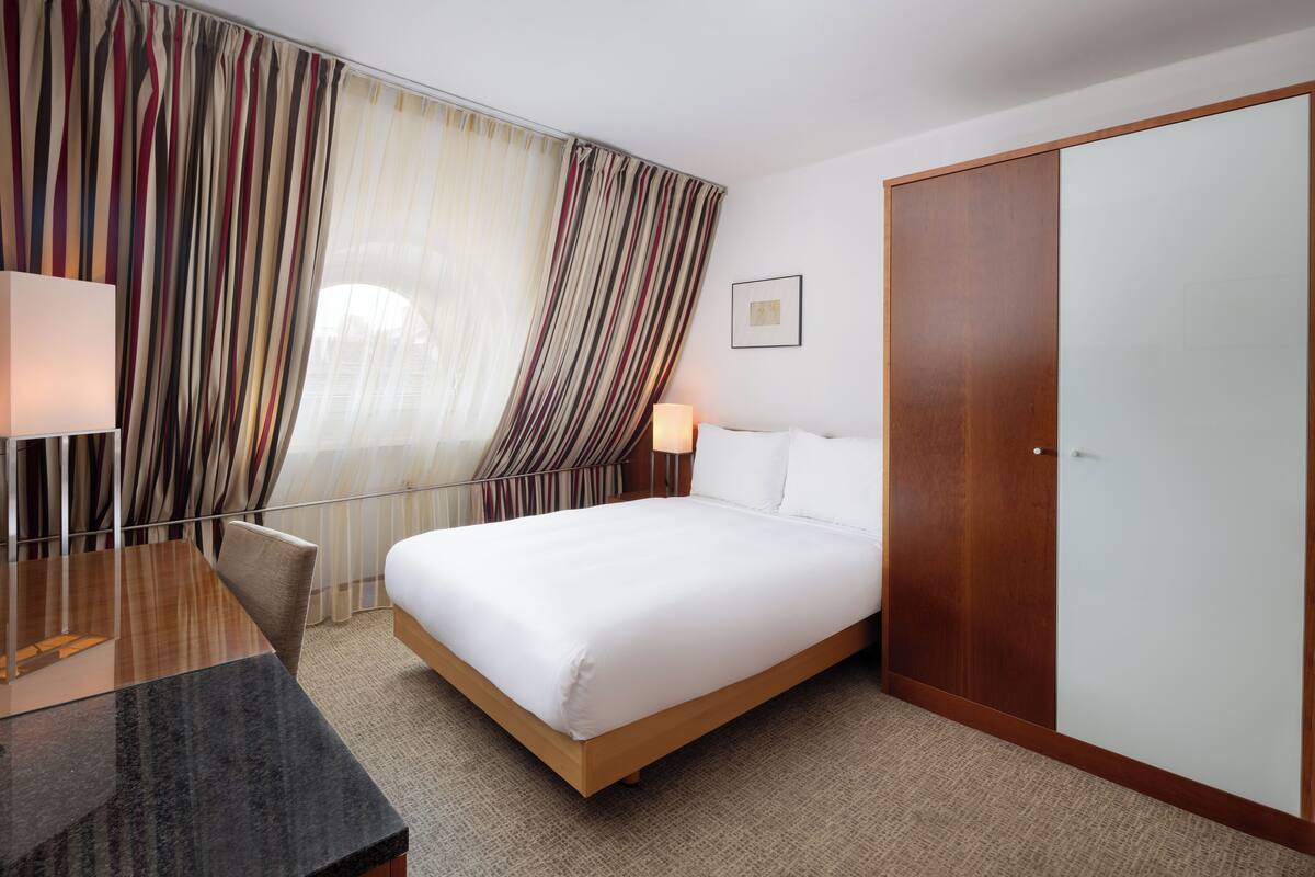 Une chambre d’hôtel comprenant un lit, un bureau, une chaise, une armoire et des rideaux.