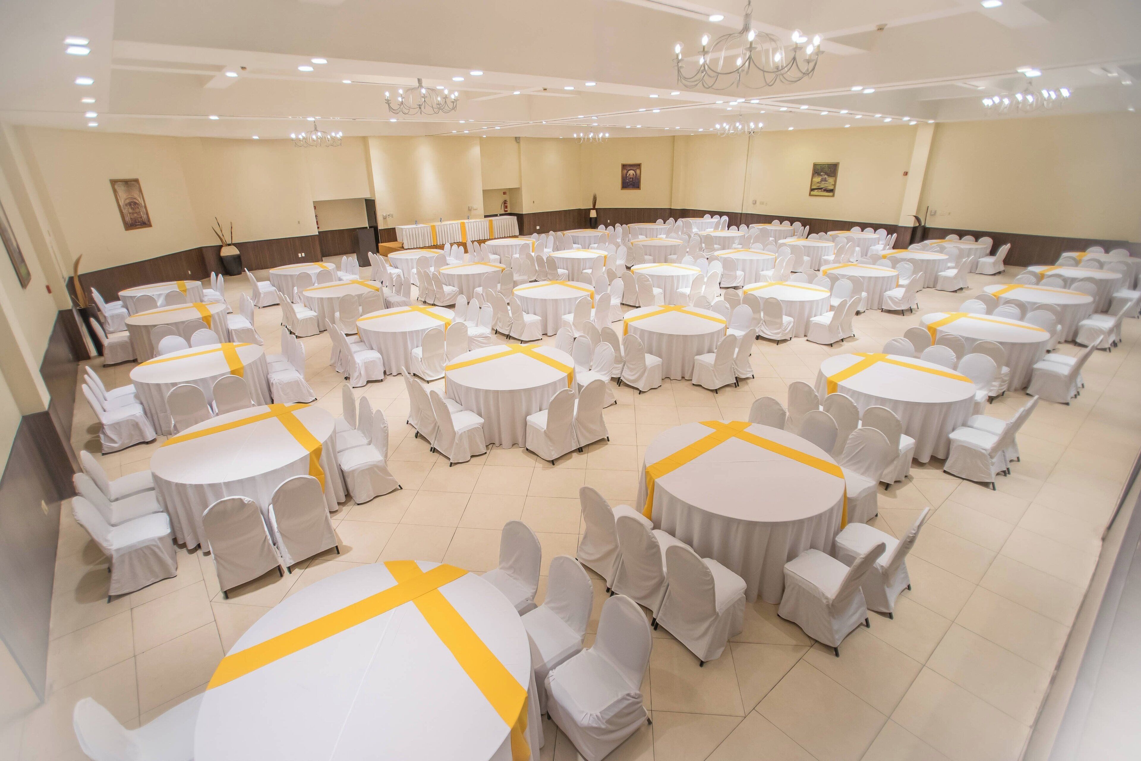 Un amplio salón de banquetes bien iluminado con varias mesas redondas y sillas, dispuestas en filas.