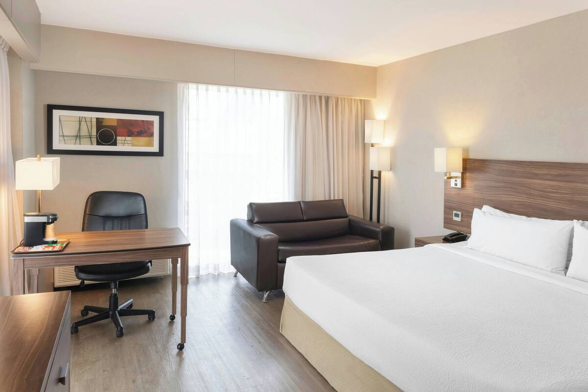 A hotel room with a large bed, a desk with a chair, a sofa, and a framed picture on the wall.