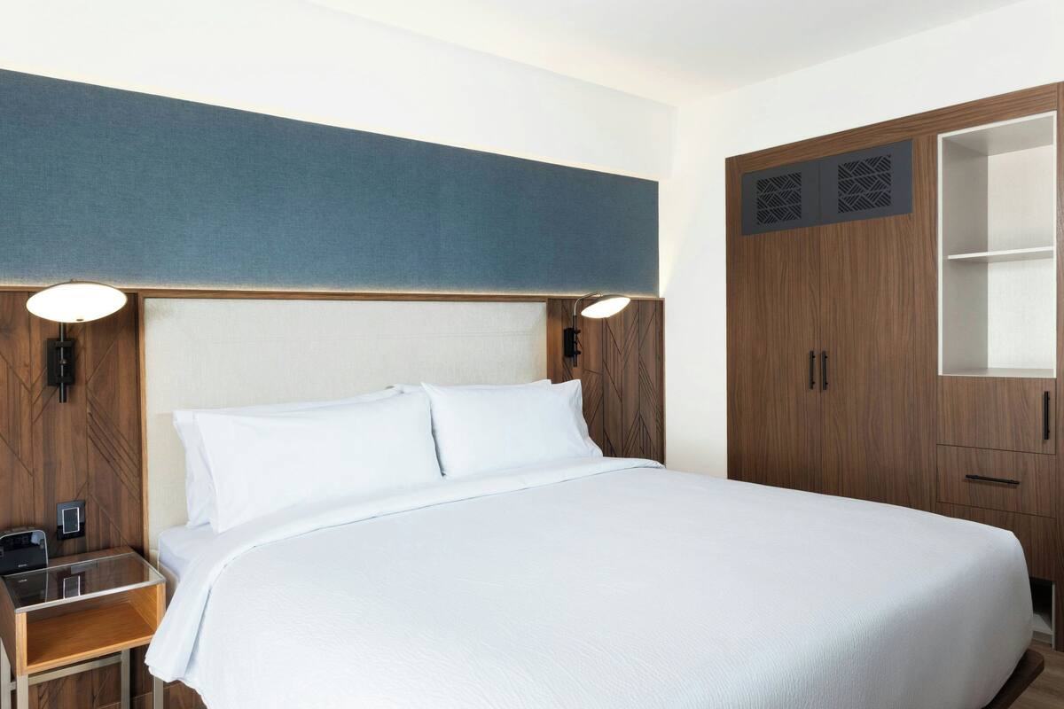 A hotel room with a large bed, wooden headboard, bedside tables, and a wardrobe.