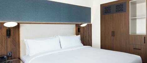 Una habitación de hotel con una cama grande, cabecera de madera, mesitas de noche y un armario.