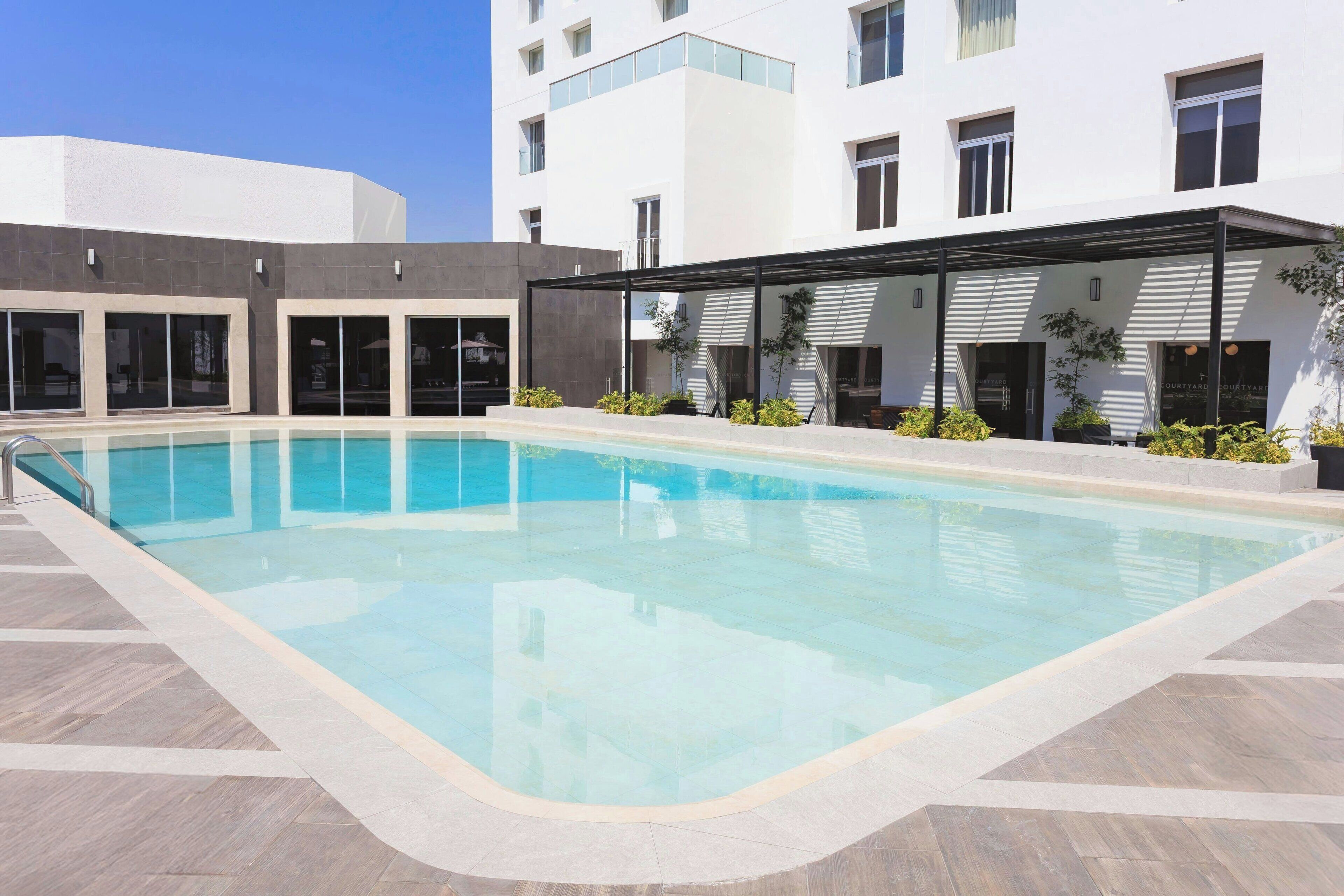 A modern building with a swimming pool, large windows, and a covered outdoor area with plants.