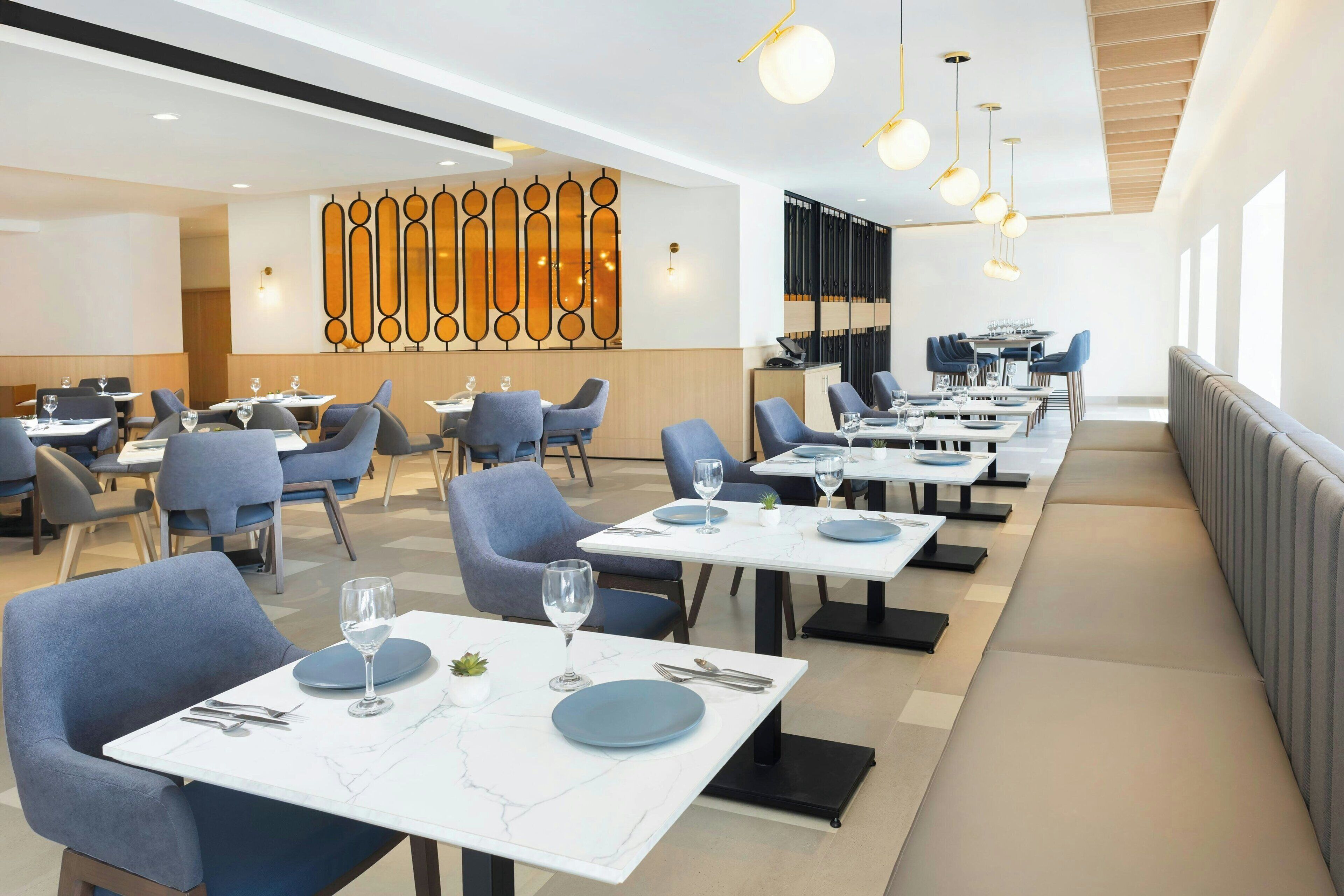 A modern dining area with tables set for two, featuring marble tops and blue plates.