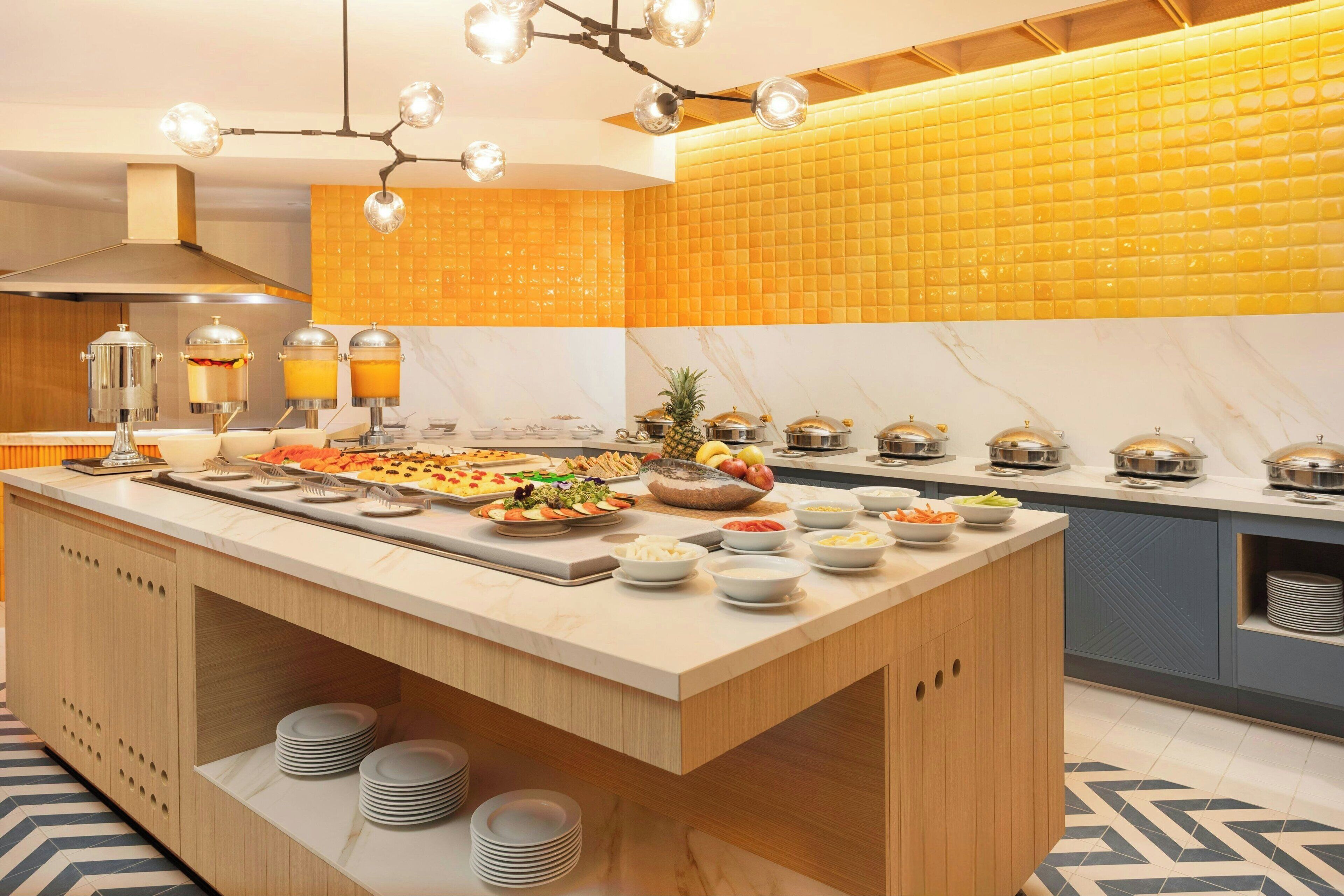 Una cocina moderna con una isla central, presentación tipo bufé de alimentos y un salpicadero con azulejos amarillos.
