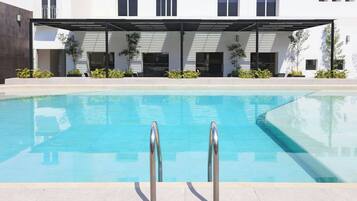 Una piscina con dos pasamanos metálicos, rodeada por un porche cubierto con asientos y plantas en macetas.