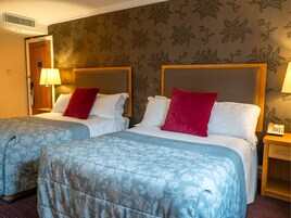 A hotel room with two beds, each with a headboard, bedside lamps, and a telephone on the nightstand.