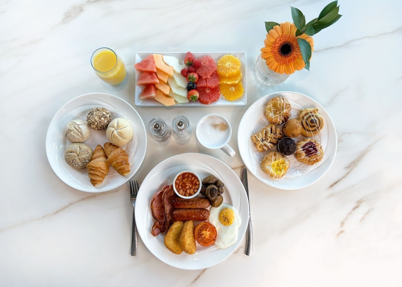 A breakfast spread with croissants, pastries, fruits, and a coffee cup on a marble table.